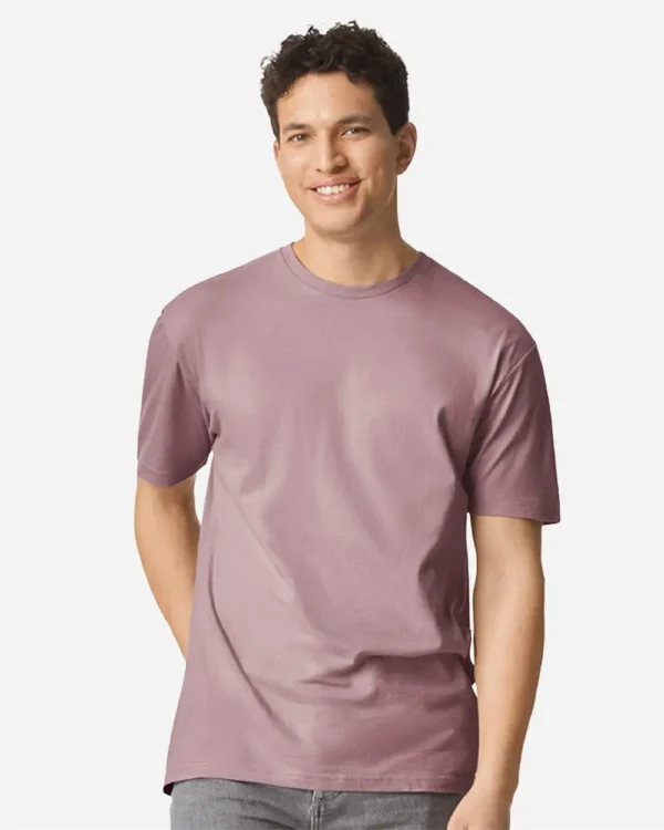 Smiling man wearing a dusty pink short-sleeve t-shirt, standing against a light background.