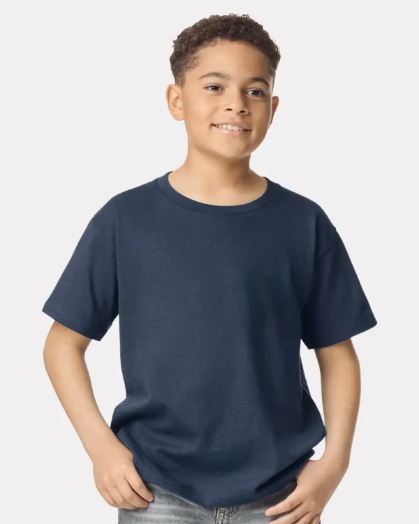 Smiling boy in a navy blue T-shirt with hands in his pockets against a light background.