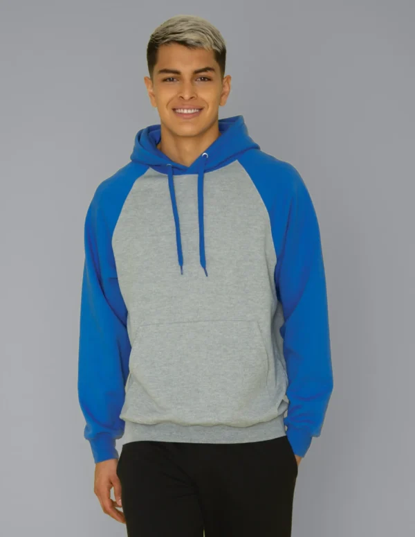 Person wearing a grey and blue hoodie, standing against a plain gray background, smiling at the camera.